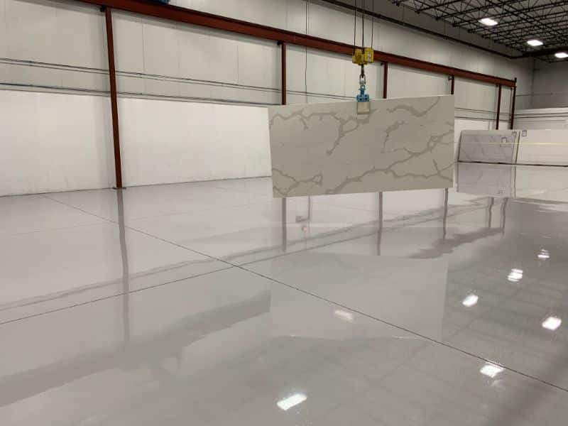 Glossy warehouse floor with a marble-patterned panel being lifted by a crane.