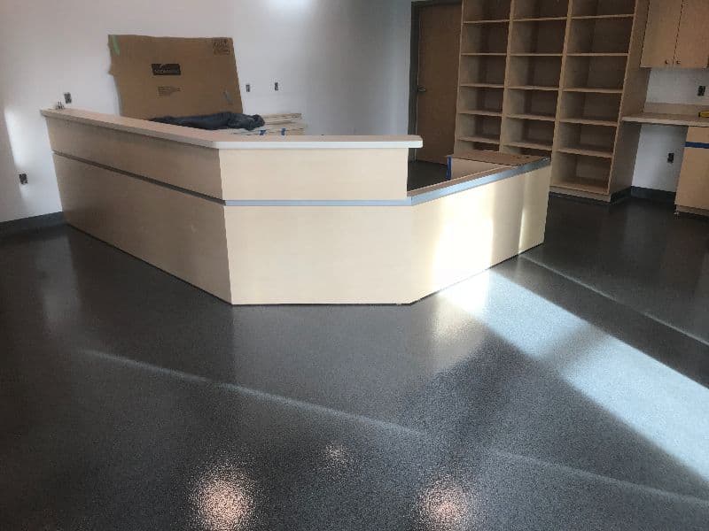 Modern reception desk in a minimalist office space with polished flooring and shelving.