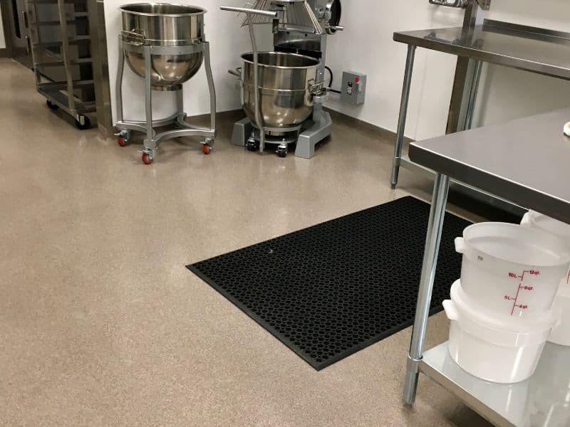 Commercial kitchen setup featuring mixing bowls, a mixer, and a rubber mat for safety.