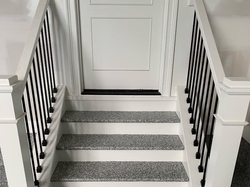 White door at the top of gray stair with black railings and textured steps.
