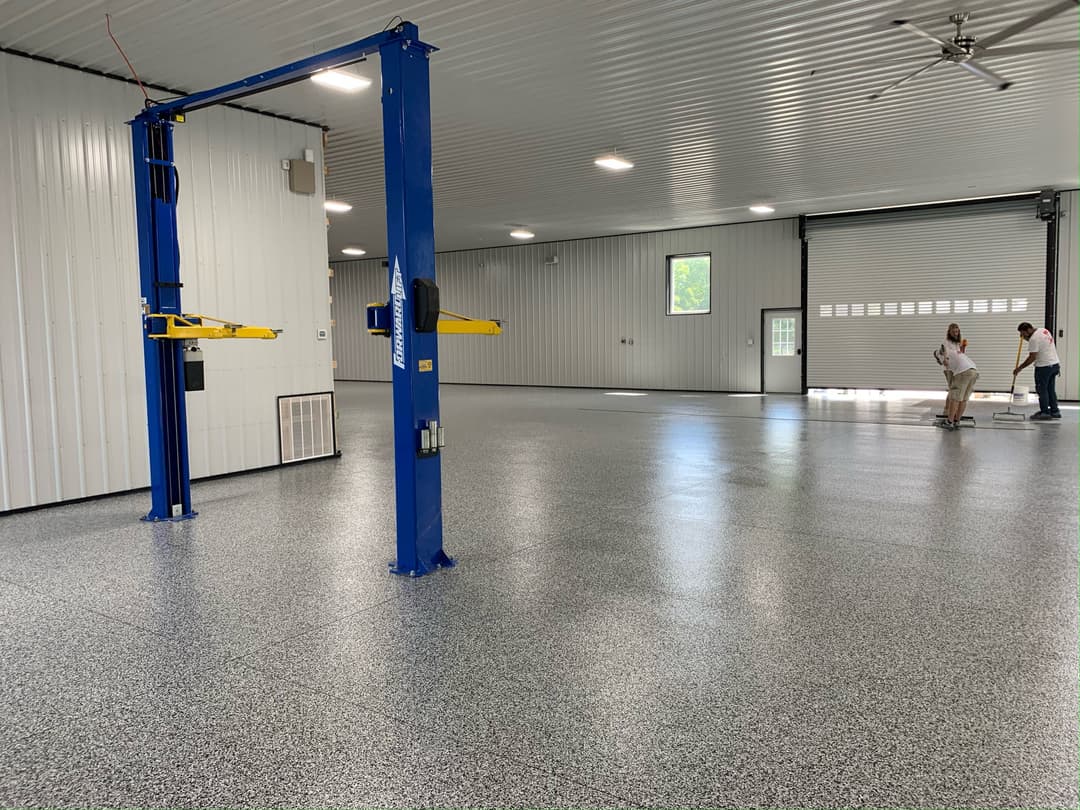 Spacious industrial garage with a blue car lift, polished floor, and workers in action.