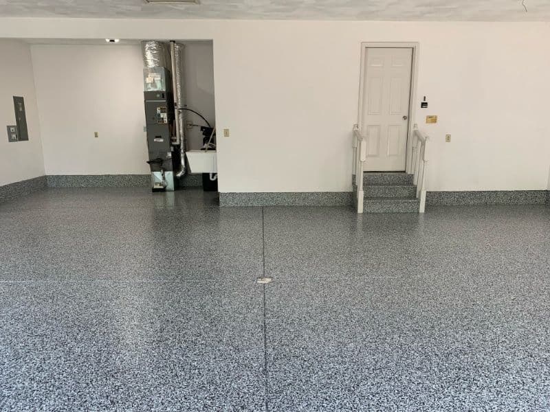 Clean garage with epoxy flooring, stairs leading to door, and HVAC unit visible.