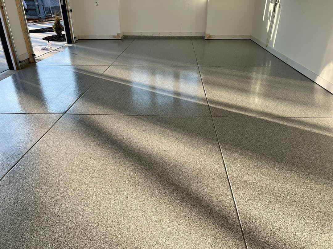 Shiny, newly finished epoxy garage floor with sunlight reflections and grey speckled design.