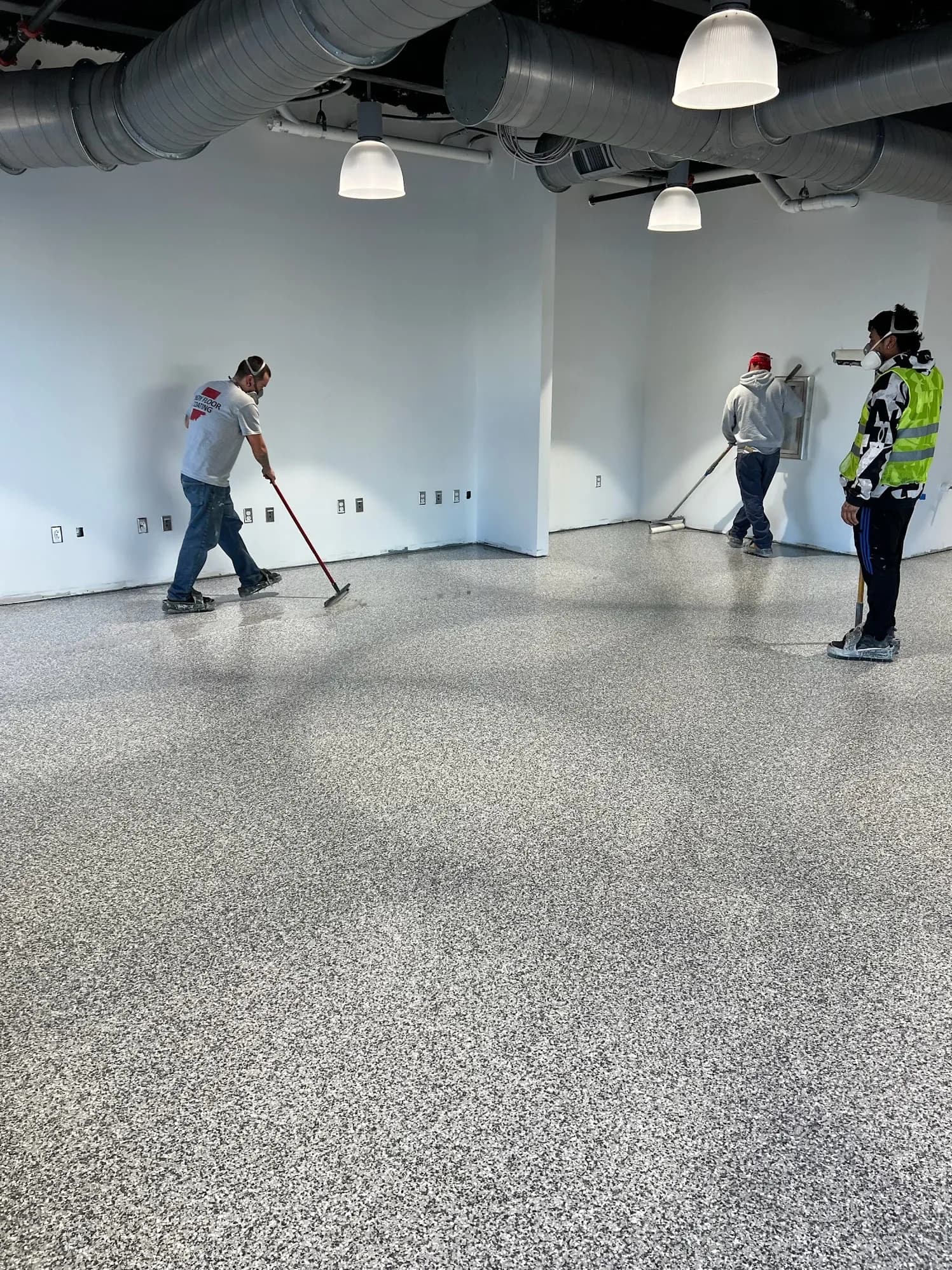 Flooring installation in a commercial space with workers applying epoxy coating.