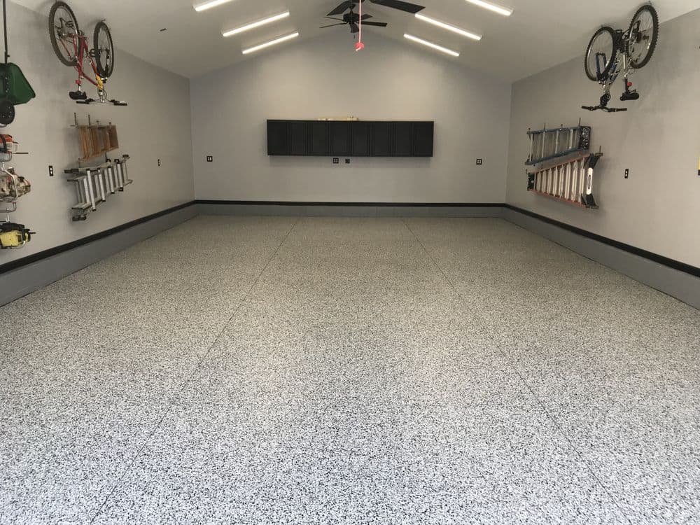 Spacious garage with gray flake flooring, wall-mounted storage, and bright lighting.