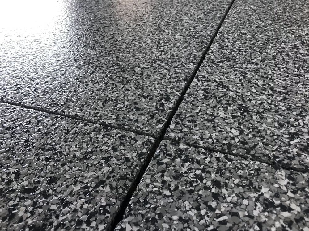Close-up of textured black and gray flooring with visible seams and reflective surface.