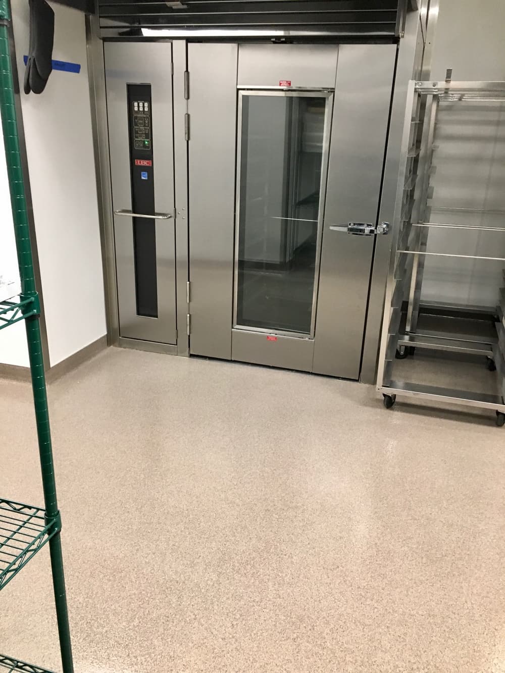 Industrial kitchen elevator with glass door, stainless steel finish, and storage shelves nearby.