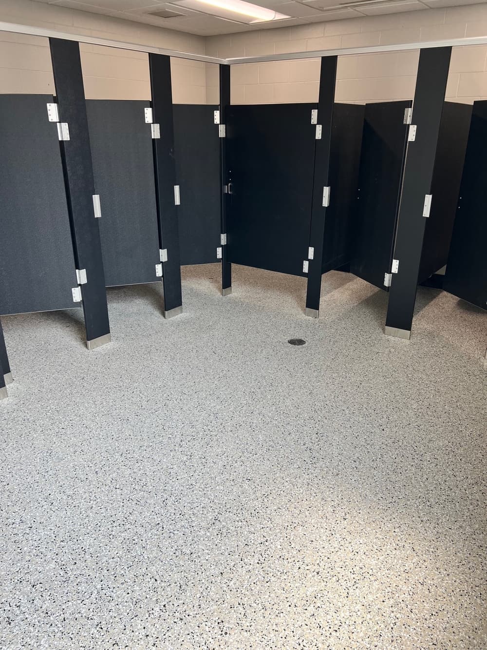 Clean public restroom with multiple black stall doors and a speckled gray floor.