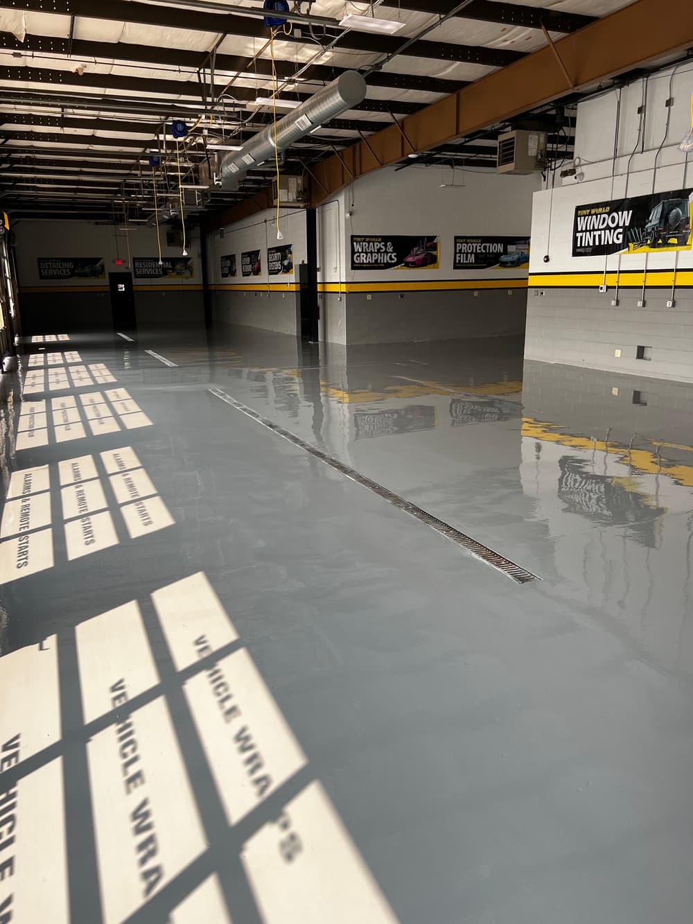 Empty commercial garage with polished gray floor, showcasing vehicle wrap and window tinting services.