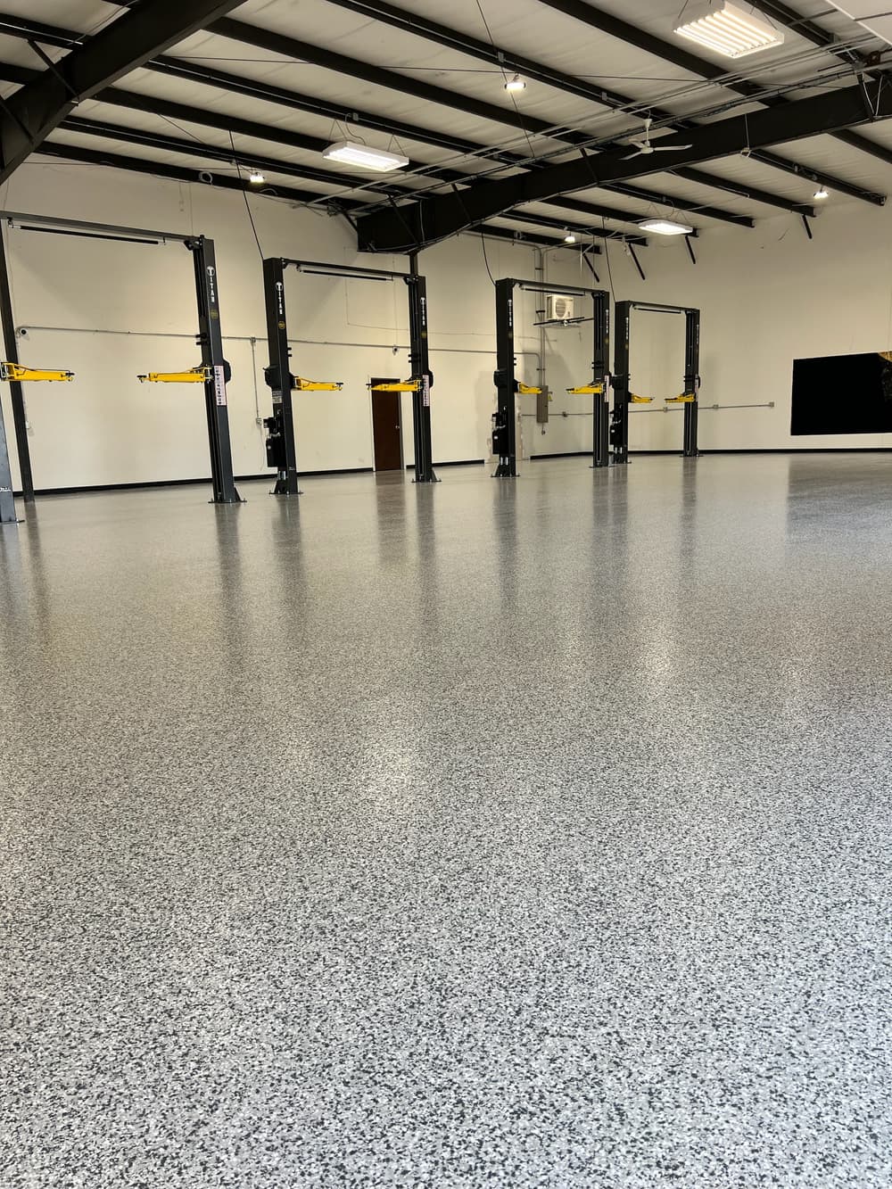 Spacious garage interior with four auto lifts and a polished speckled floor.