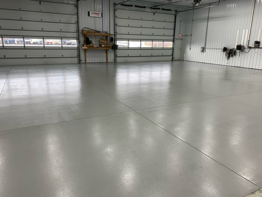 Empty industrial garage with shiny gray epoxy flooring and large overhead door.
